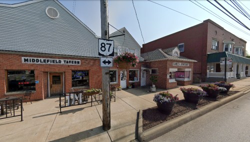 Street view of Middlefield Tavern and a nearby shop, featuring outdoor seating and flower planters along the sidewalk.