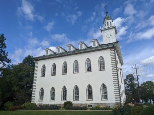 Historic white church with arched windows and a clock tower, set against a blue sky with scattered clouds.