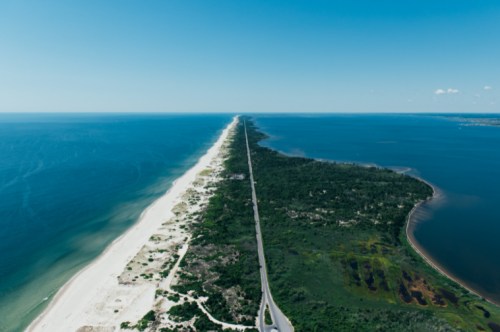 Aerial view of a long, narrow strip of land bordered by blue ocean on one side and green vegetation on the other.