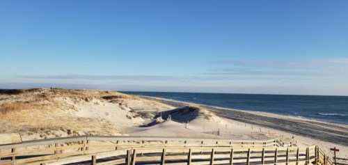 A serene beach scene with golden sand dunes, gentle waves, and a clear blue sky.