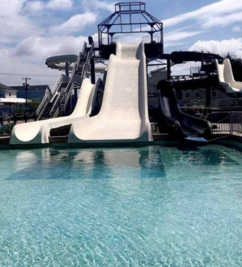 A water park featuring multiple slides and a clear blue pool under a sunny sky.