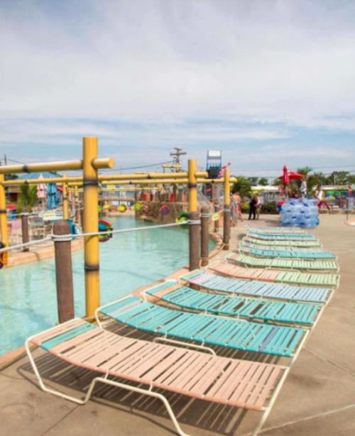 A colorful water park with lounge chairs lined up beside a pool and play structures in the background.