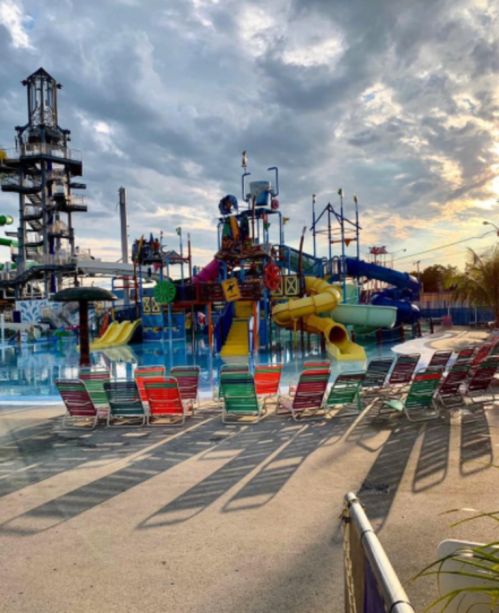 Colorful water slides and a pool area with lounge chairs under a cloudy sky at a water park.