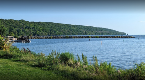 A serene lake view with green hills in the background, a rocky pier, and calm water under a clear blue sky.