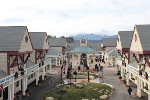 A shopping plaza with festive decorations, featuring buildings, people, and mountains in the background under a cloudy sky.