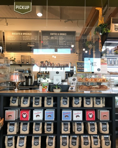 A cozy café counter displaying coffee drinks, baked goods, and a menu board, with bags of coffee on shelves.