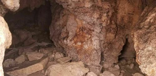 A rocky cave interior with uneven walls and scattered stones on the ground, creating a natural, rugged environment.