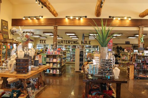 Interior of a gift shop featuring wooden beams, shelves of products, and a sign reading "The Watering Hole."