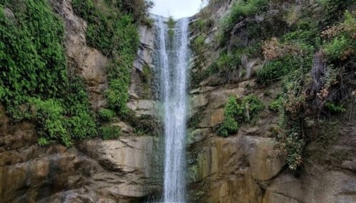 A serene waterfall cascading down a rocky cliff, surrounded by lush green vegetation.