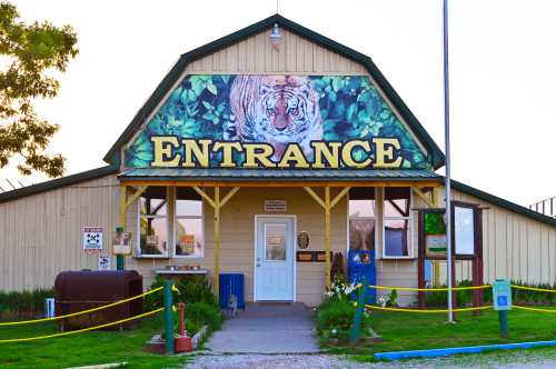 A building with a large "ENTRANCE" sign and a tiger mural, surrounded by greenery and a yellow safety barrier.