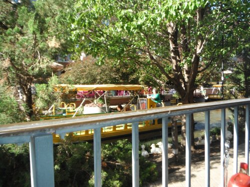 A view of a riverboat surrounded by lush greenery and trees, with people enjoying the scenery.