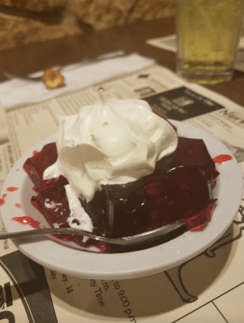 A small dish of red jelly topped with whipped cream, placed on a table with a menu in the background.