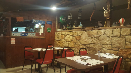 Cozy restaurant interior with stone walls, wooden decor, and red chairs around tables, featuring vintage items on display.