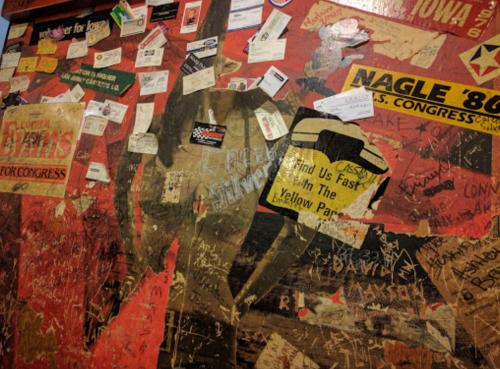 A textured wall covered in various stickers, posters, and handwritten notes, showcasing a mix of colors and designs.
