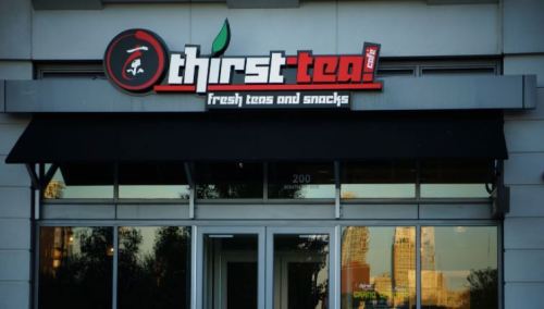 Sign for "thirst tea" featuring fresh teas and snacks, with a modern storefront and large windows.