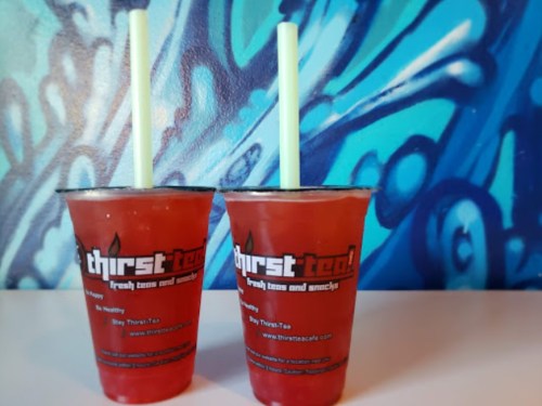 Two cups of iced tea with green straws, placed on a table against a colorful blue mural background.