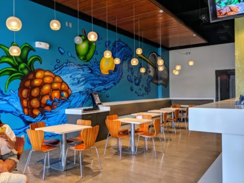 Brightly lit restaurant interior featuring colorful fruit mural, wooden tables, and modern pendant lights.