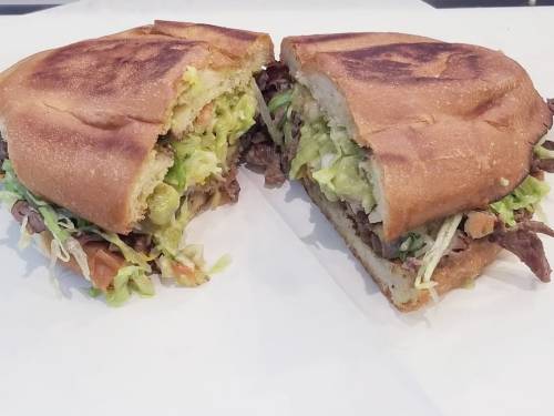 A halved sandwich filled with shredded lettuce, tomatoes, and sliced beef on toasted bread.