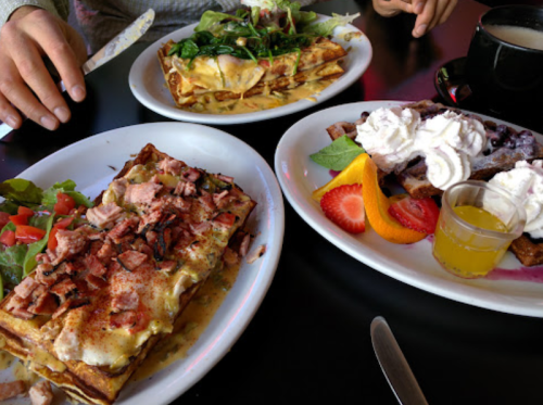 A table with three plates of food: a savory dish with ham and cheese, a sweet dish with whipped cream and fruit, and a salad.