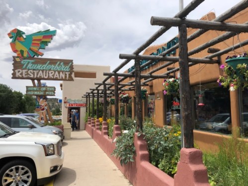 Exterior of Thunderbird Restaurant featuring colorful signage, a wooden trellis, and flower planters along the walkway.