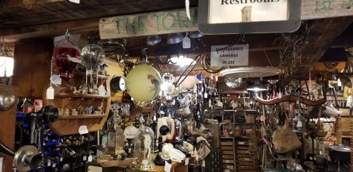 A cluttered antique shop filled with various vintage items, lamps, and signs, including a restroom sign.