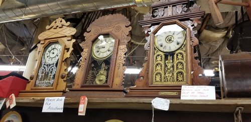 Three vintage wooden clocks with intricate designs displayed on a shelf in a shop.