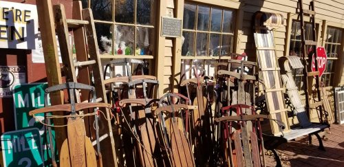 A collection of vintage wooden sleds displayed outside a building with large windows and various signs.
