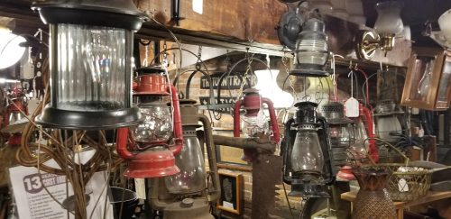 A collection of vintage lanterns hanging in a rustic shop, showcasing various styles and colors.