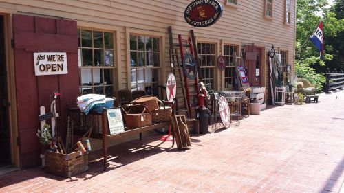 A quaint antique shop exterior with various vintage items displayed outside, including baskets, signs, and furniture.