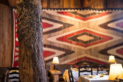 Cozy restaurant interior featuring a large patterned wall hanging and wooden decor, with tables and soft lighting.