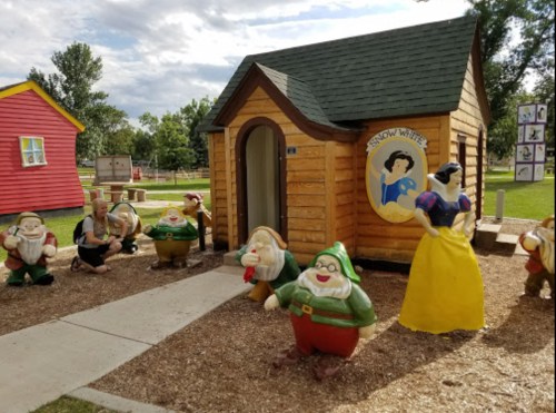 A whimsical scene featuring a small wooden house and colorful Snow White and the Seven Dwarfs statues in a park.