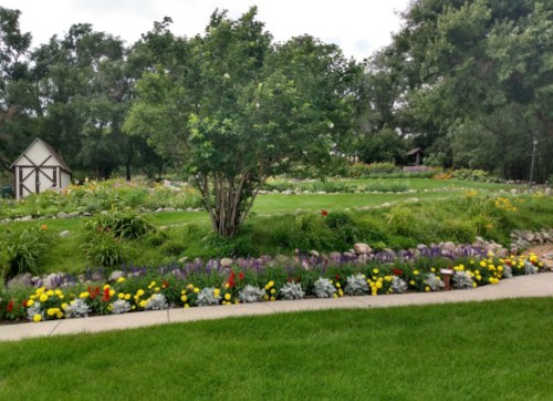 A lush garden with colorful flowers, neatly arranged along a winding path and surrounded by greenery and trees.
