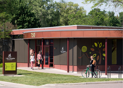 A modern building with a sign reading "750" and colorful tree designs, with people walking and one on a bicycle.