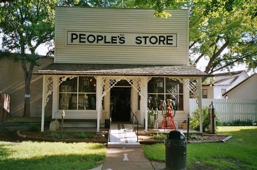 A quaint storefront labeled "The People's Store," featuring a porch and surrounded by greenery.