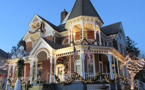 A beautifully decorated Victorian house adorned with holiday lights and wreaths, set against a twilight sky.
