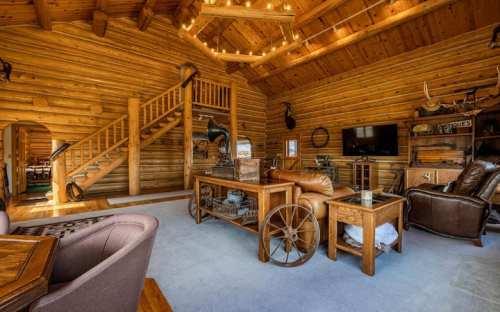 Cozy log cabin interior with wooden beams, a staircase, and rustic furniture, creating a warm, inviting atmosphere.