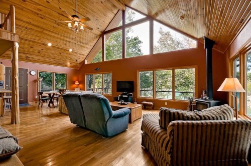 Cozy living room with wooden ceiling, large windows, and comfortable seating, overlooking a scenic outdoor view.