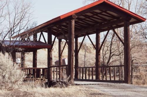 A wooden pavilion with a red roof, surrounded by bare trees and a gravel path.