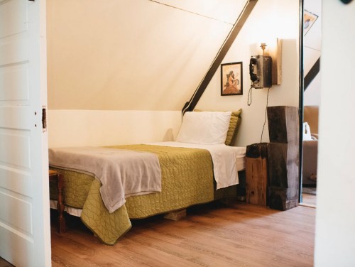 Cozy bedroom with a bed, green quilt, wooden accents, and vintage phone against a slanted wall. Warm, inviting atmosphere.