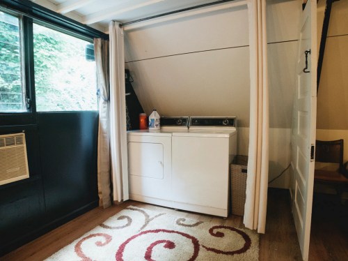A laundry area with a washer and dryer, partially hidden by curtains, next to a window and a decorative rug.