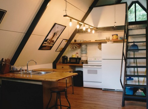 Cozy kitchen with wooden island, white appliances, and a staircase, featuring modern lighting and rustic decor.