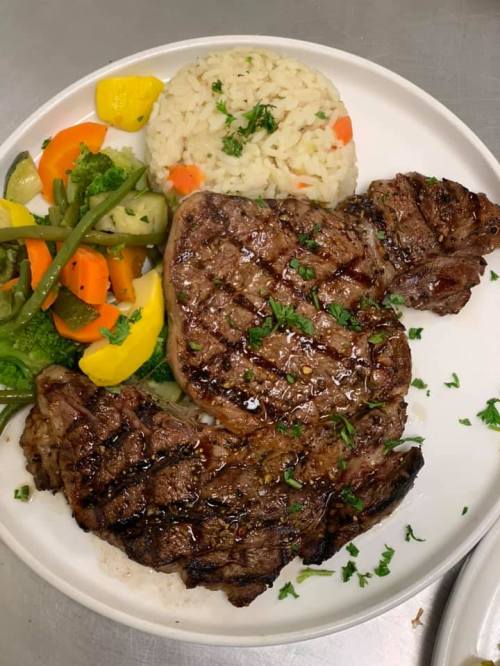 A plate with grilled steak, seasoned rice, and a mix of colorful vegetables.