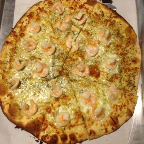 A pizza topped with shrimp, cheese, and herbs, sliced into equal pieces on a baking tray.