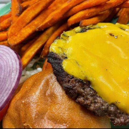 A close-up of a cheeseburger with melted cheese, served with sweet potato fries and a slice of red onion.