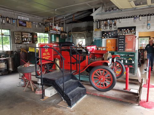 A vintage red car displayed in a rustic garage filled with tools and memorabilia.