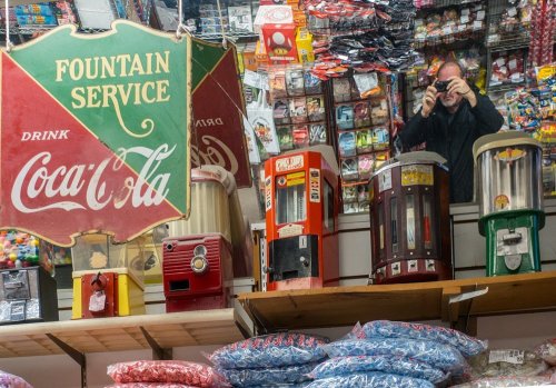 A vintage Coca-Cola sign reflects in a shop filled with old vending machines and colorful candy.