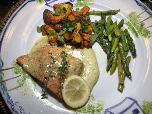 A plate featuring salmon with lemon and herb sauce, roasted vegetables, and asparagus.