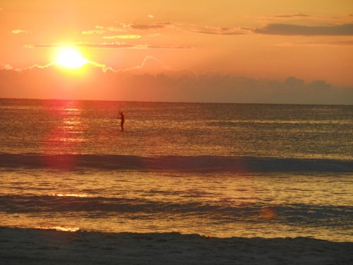 A serene sunset over the ocean, with a silhouette of a person standing in the water.