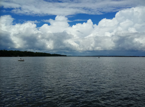 A serene lake scene with a boat on the water, under a sky filled with fluffy clouds and blue hues.