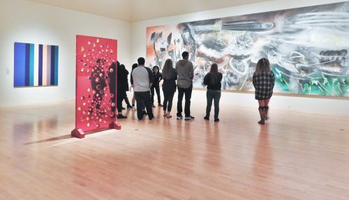 Visitors admire contemporary art in a spacious gallery featuring colorful paintings and a unique sculpture.